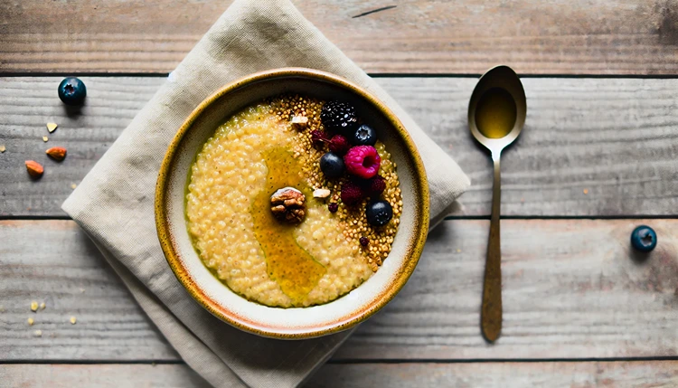 Warm amaranth porridge topped with maple syrup, berries, and nuts in a bowl on a rustic wooden table